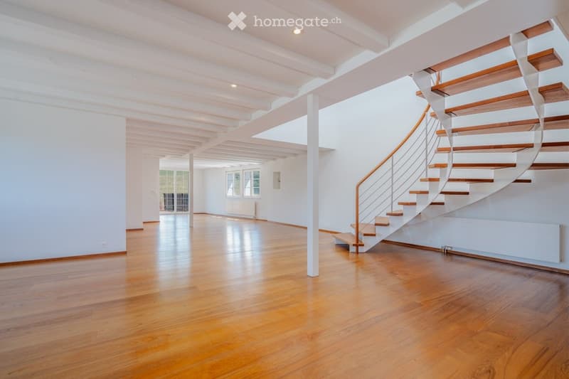 Bright, open hallway with polished wooden flooring, white walls, and a modern wooden staircase leading upwards.