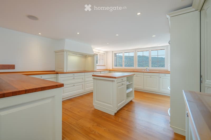 Bright, airy kitchen with white cabinets, wooden countertops, and hardwood flooring. Large windows offer a scenic view.