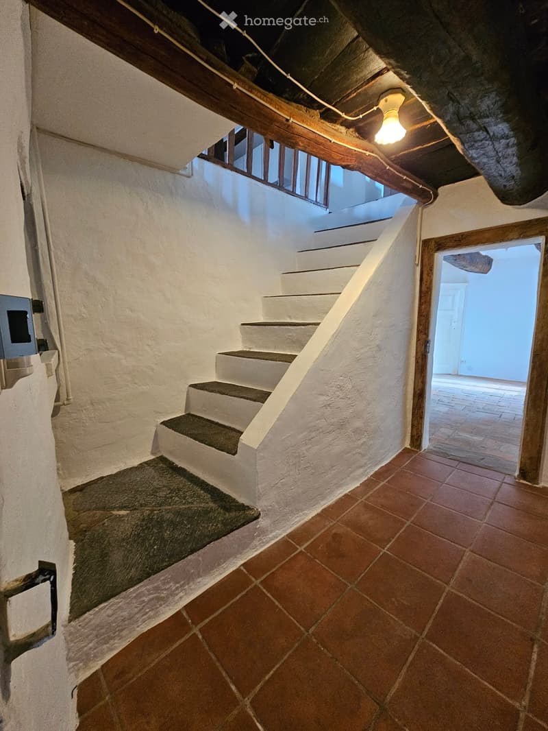 Staircase, white painted walls, terracotta tiled floor, light fixture hanging from ceiling, wooden handrail