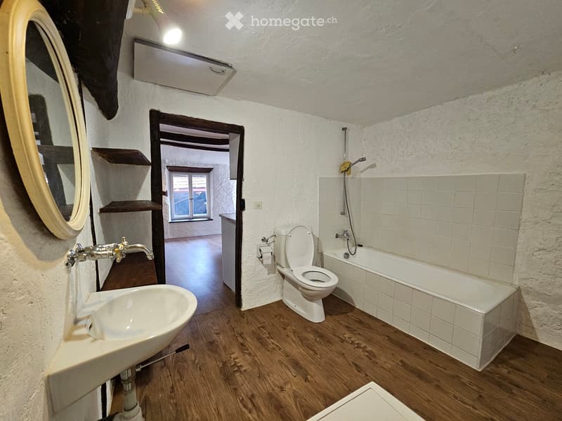 bathroom with white bathtub, white sink, wooden floor, open door to another room with window