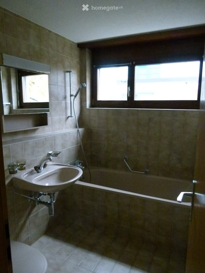 Bathroom with a sink, bathtub, mirror, and showerhead. The room features tiled walls and a window providing natural light.