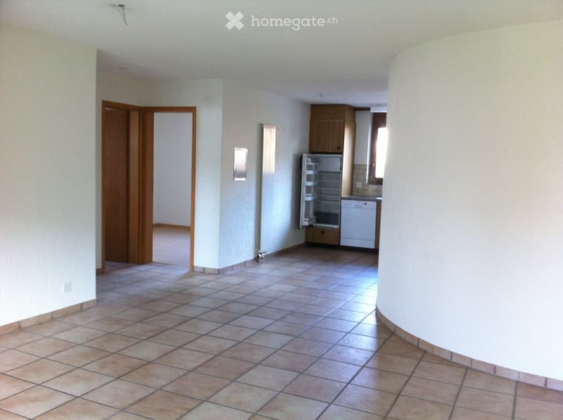 Open-plan area with tiled flooring, a refrigerator, dishwasher, and cabinetry visible in the background.
