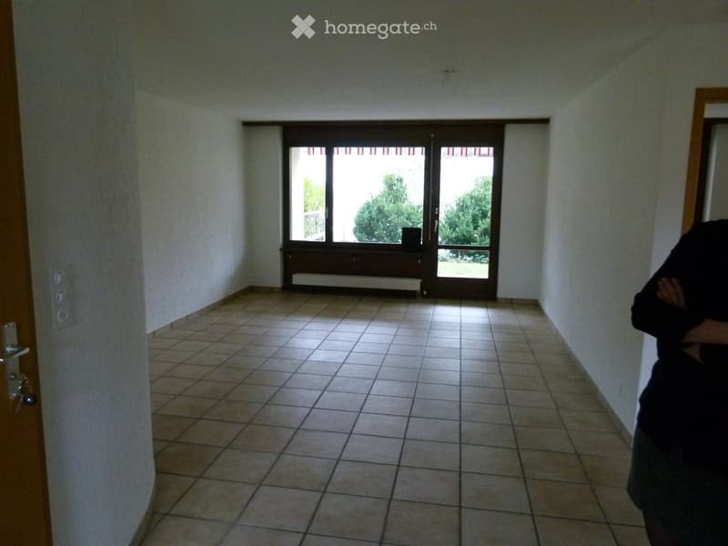 Empty hallway with tiled floor, white walls, and a large window at the end, allowing natural light to enter.