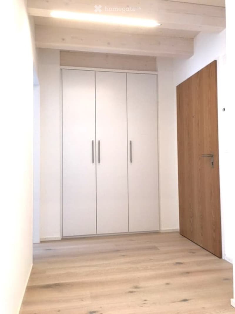 Empty room with white walls, light wooden floor, white built-in wardrobe, and a wooden door.