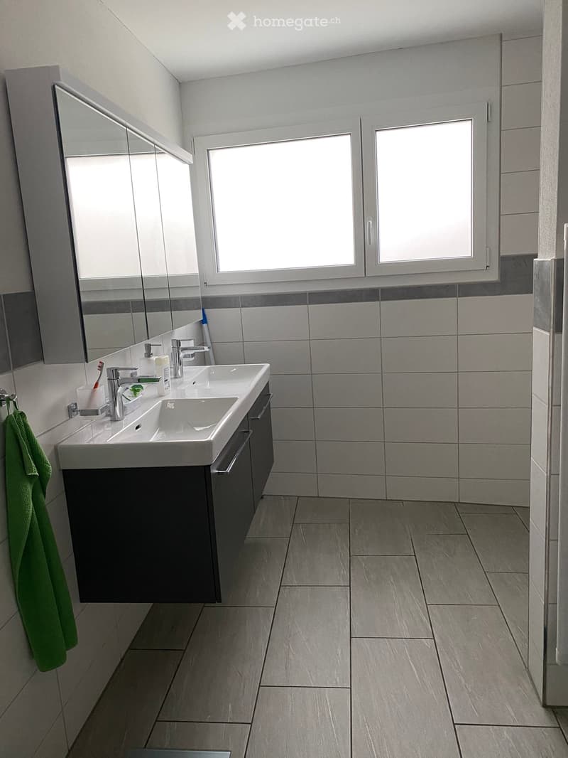 Modern bathroom with a double sink, large mirror, tiled walls, and a green towel hanging on the side.