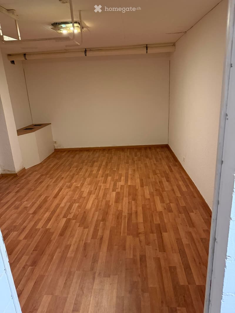 Empty room with wooden flooring and white walls, featuring a small built-in shelf on one wall and a ceiling light fixture.