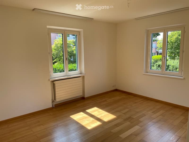 Empty room with wooden flooring, white walls, and two windows with white frames. A radiator is visible under one window.