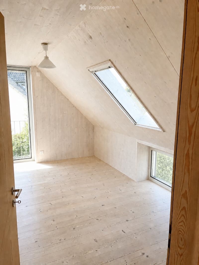 Empty attic room with wooden walls, floor, and ceiling, featuring skylight windows and a hanging light fixture.