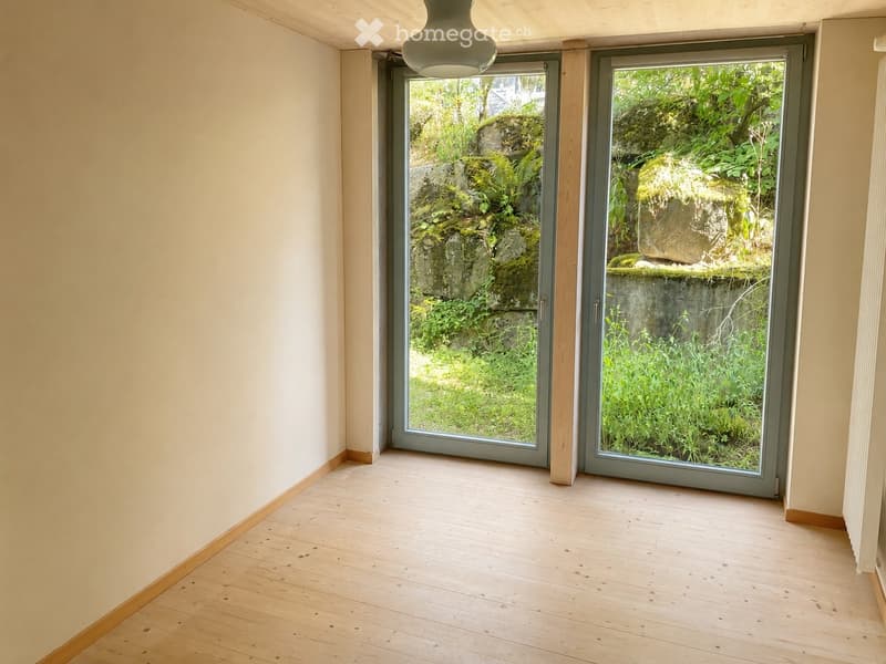 Empty room with light wooden flooring and large sliding glass doors leading to a green outdoor area.