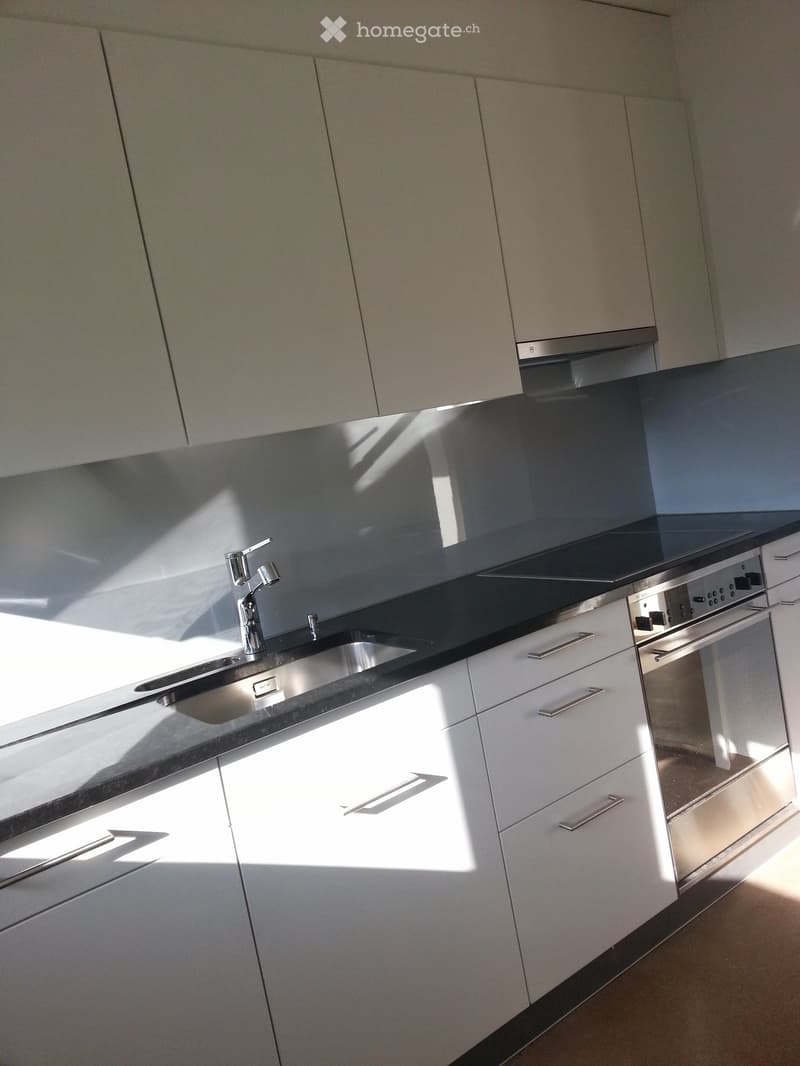 Modern kitchen with white cabinets, stainless steel sink, and built-in oven. Sunlight streams in from a window, casting shadows on the countertops.