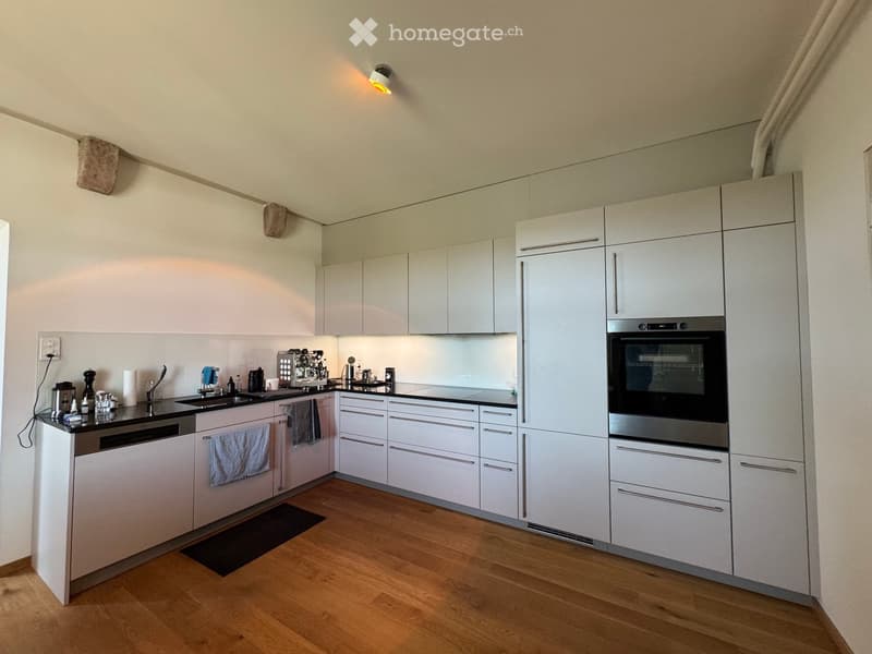 Modern kitchen with white cabinets, stainless steel appliances, wooden flooring, and a coffee machine on the counter.