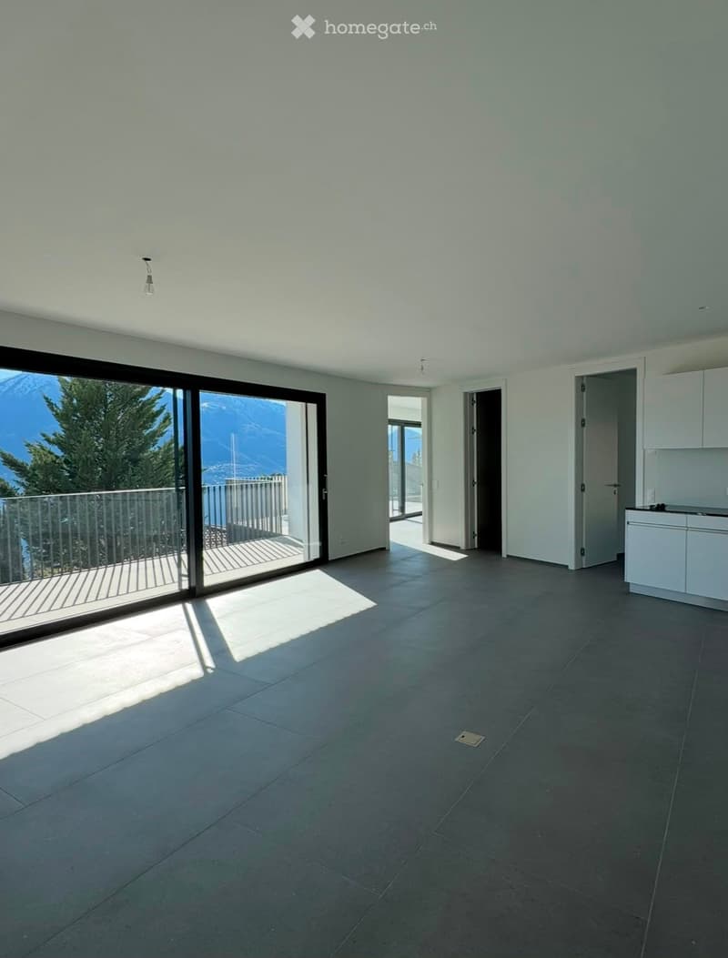 Empty room with large sliding glass doors leading to a balcony, tiled floor, white walls, and a view of mountains and trees.