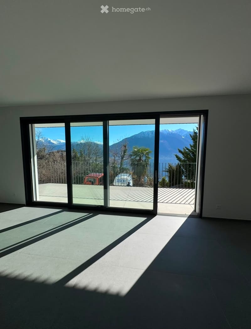 Empty room with large sliding glass doors leading to a balcony with a scenic mountain view. The room has tiled flooring and is brightly lit by natural sunlight.