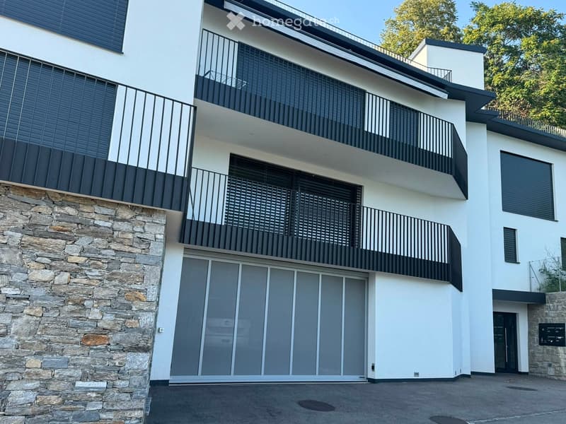 Modern two-story house with white and black exterior, stone base, large sliding glass doors, and multiple balconies with black railings.