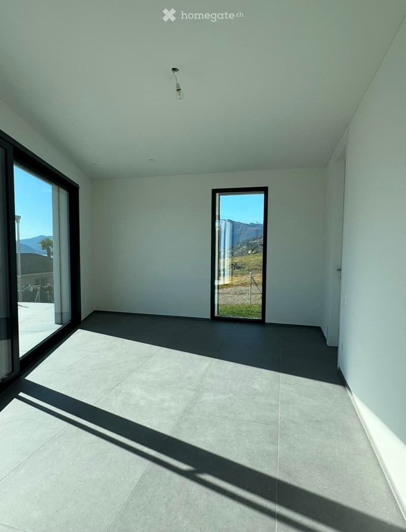 Empty room with light grey walls, dark grey tiled floor, and large windows offering a scenic view of a landscape.