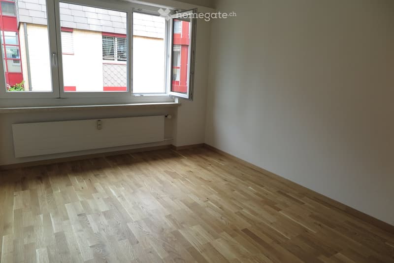 Empty room with light wooden flooring, white walls, and large windows with open shutters, allowing natural light to fill the space.