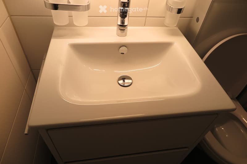 Modern bathroom sink with a sleek, white countertop and chrome faucet, integrated into a dark-toned cabinetry.