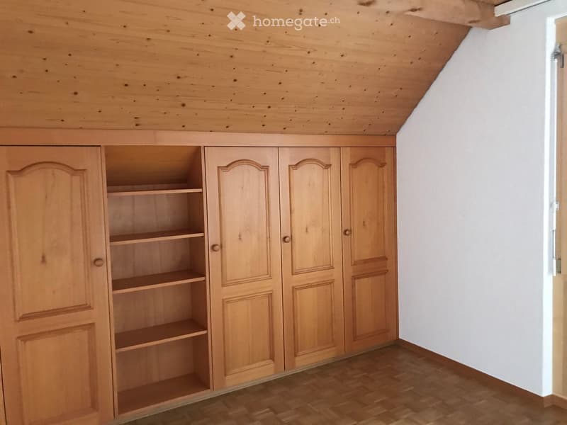 Empty room with wooden floor, white walls, and built-in wooden wardrobe with shelves and closed doors.
