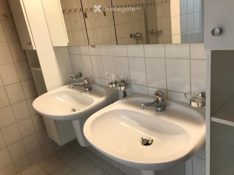 Modern bathroom with two white sinks, chrome faucets, a large mirror, and two glass cups on the counter.