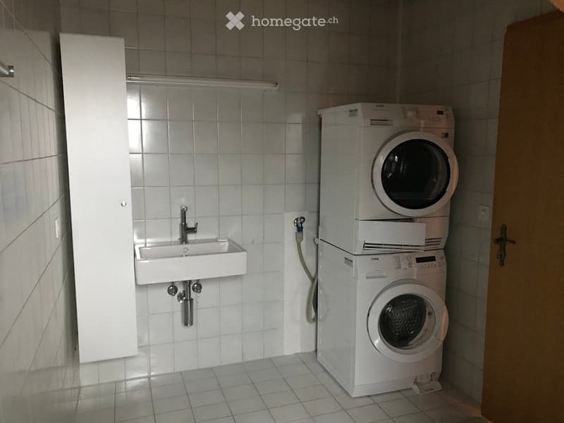 Bathroom with a white sink, a stacked washing machine and dryer, and tiled walls and floor.