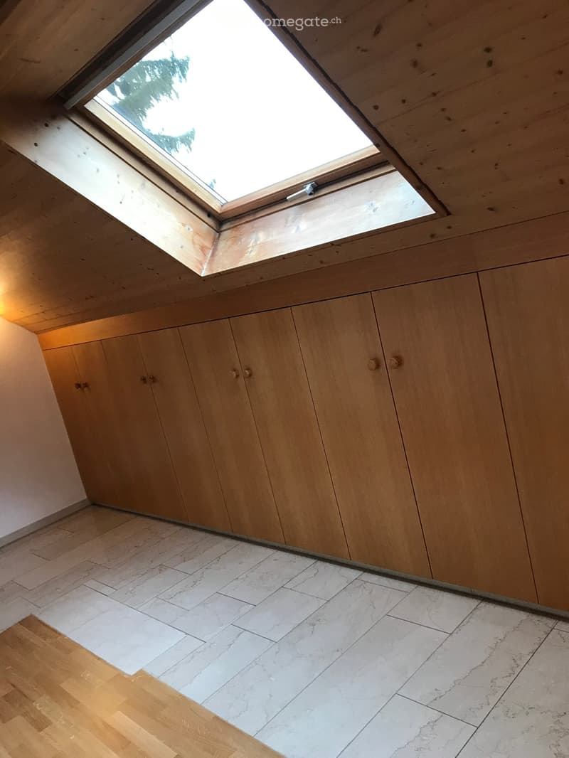 An unfurnished room with wooden walls, a skylight window, and a mix of wooden and marble flooring.