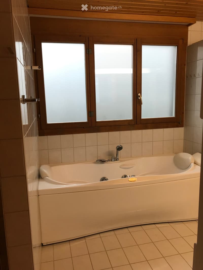 Bathroom with a large bathtub, tiled walls and floor, and a window with wooden frame above the tub.