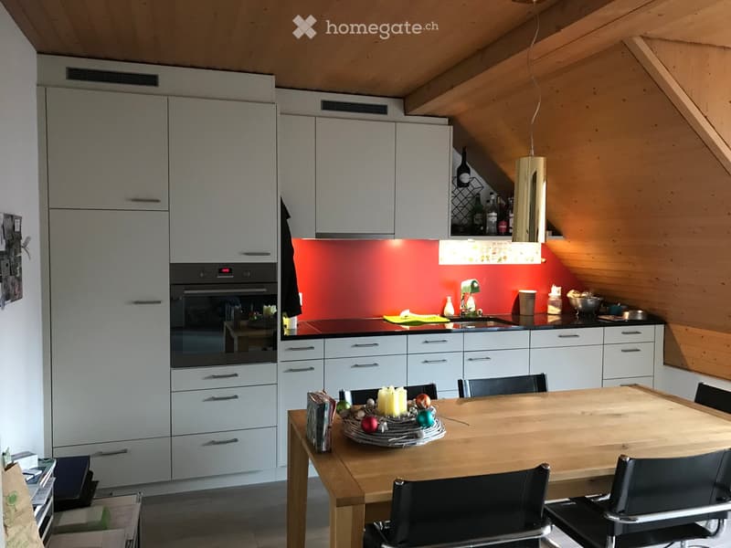 Modern kitchen with white cabinets, stainless steel appliances, a red backsplash, and a wooden dining table with chairs.