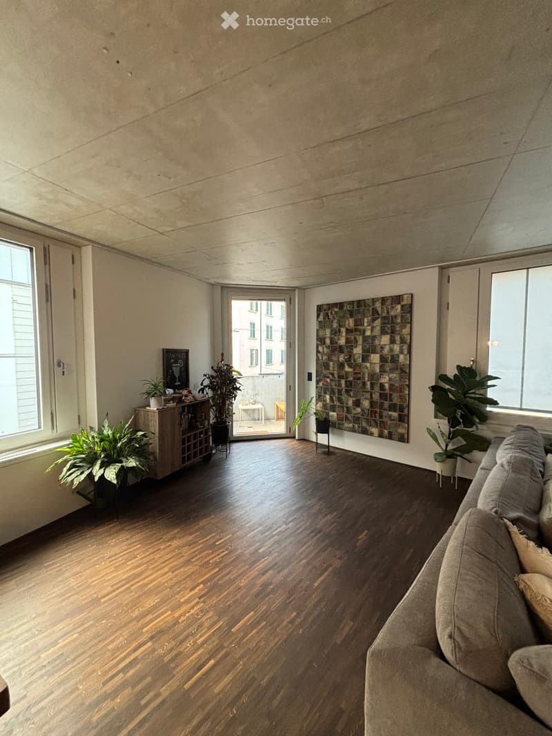 Living room with wooden flooring, large windows, a sofa, a small table with potted plants, and an art piece on the wall.