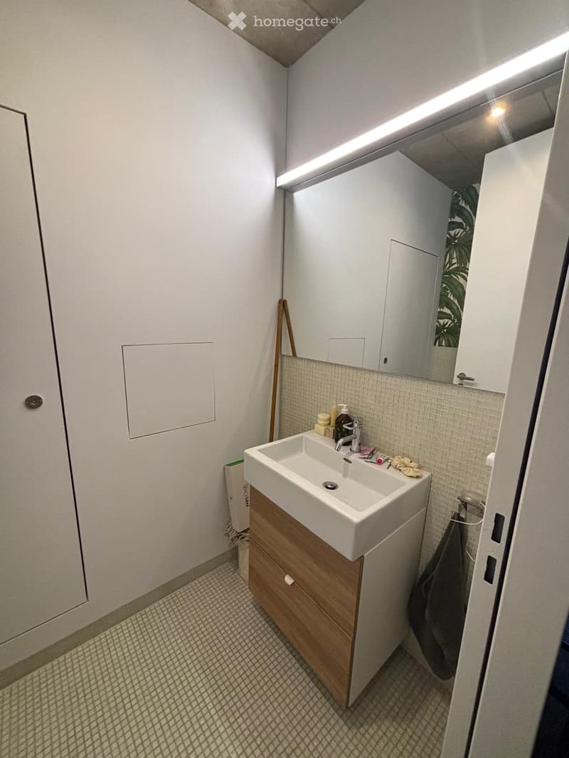 Modern bathroom with a white sink, wooden cabinet, mirror, and tiled walls.