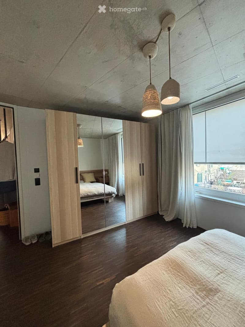 Modern bedroom with wooden flooring, large mirror wardrobe, bed, pendant lights, and large window with view.