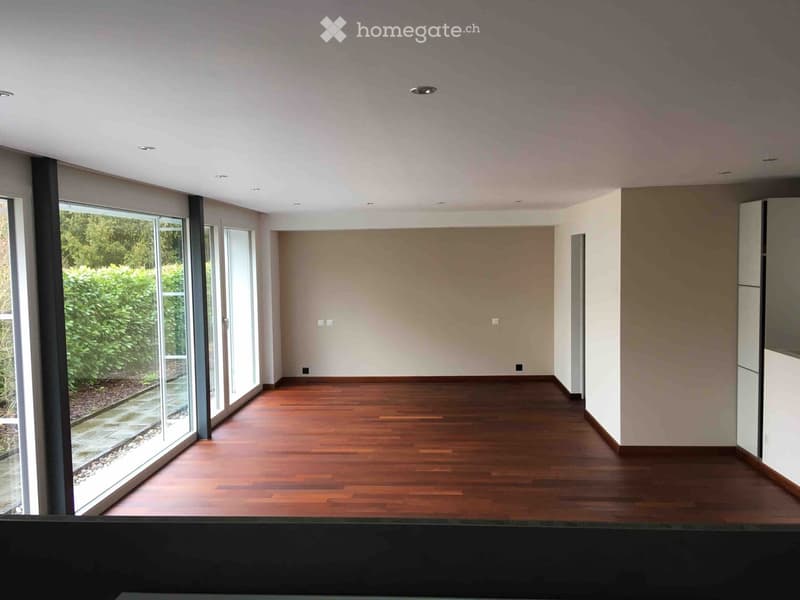 Empty room with wooden flooring, large windows, and neutral-colored walls.
