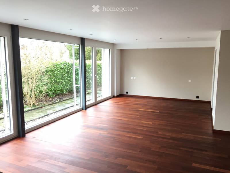Empty room with wooden flooring, large glass sliding doors leading to a garden, and white walls.