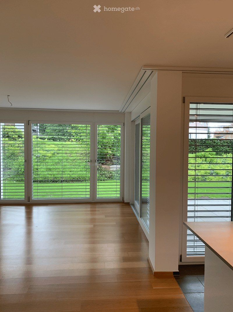 Bright, empty room with large glass doors and windows, wooden flooring, and white walls.