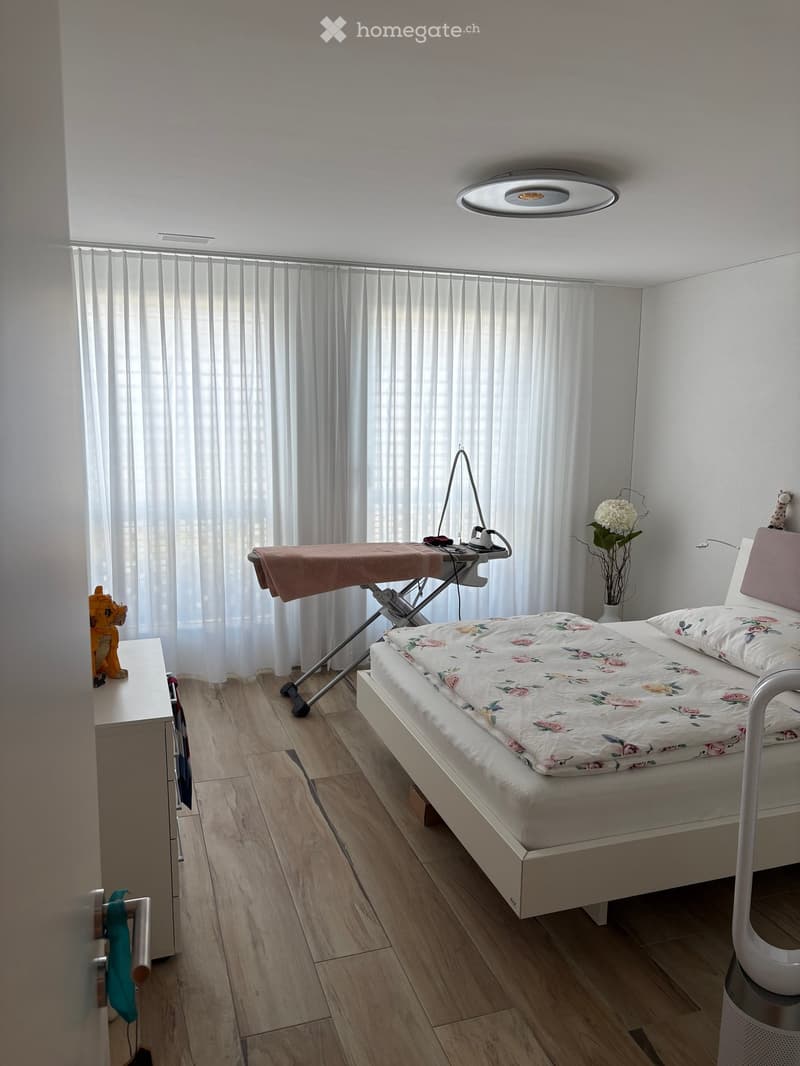 Bedroom with a bed, nightstand, lamp, ironing board, iron, flower vase, and a toy on the nightstand.