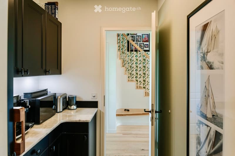 Modern kitchen with marble countertop, black cabinets, kitchen appliances, a bench near the staircase, picture frame on the wall