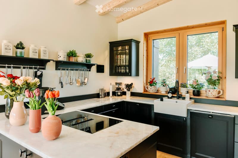 marble countertops, black cabinets, gas stove, dishwasher, kitchen island, window with potted plants