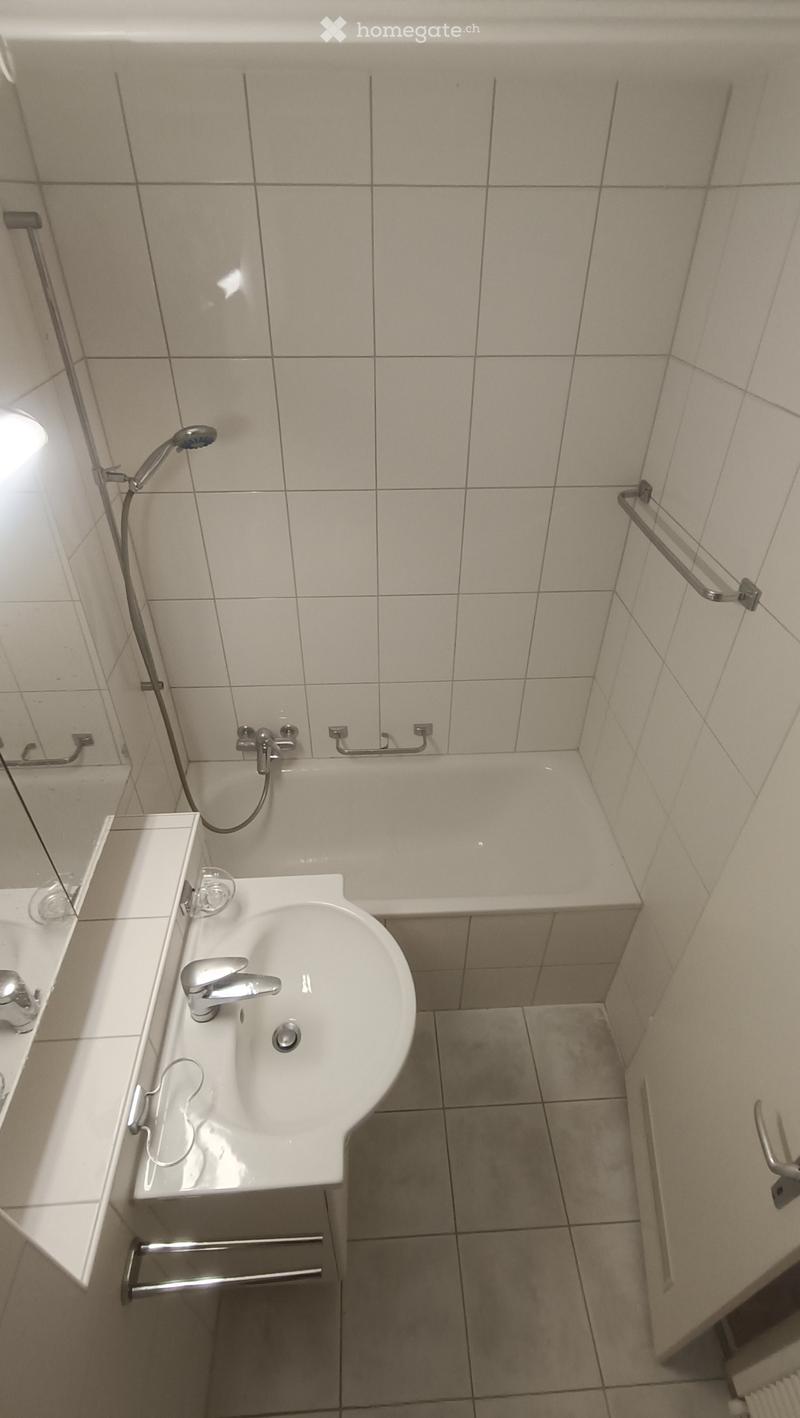 Clean bathroom with a white sink, bathtub, and showerhead. The walls and floor are tiled in light beige.