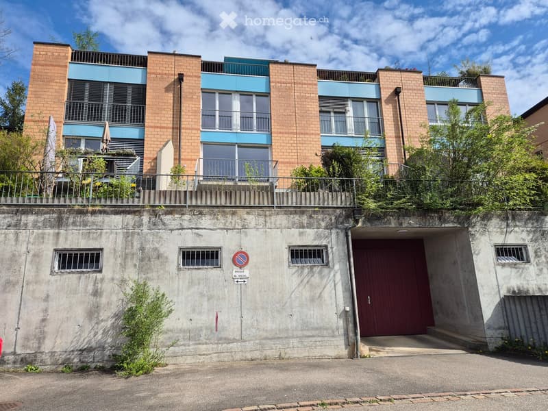 Multi-story residential building with brick and blue panel facade, balconies, and a gated underground parking area.