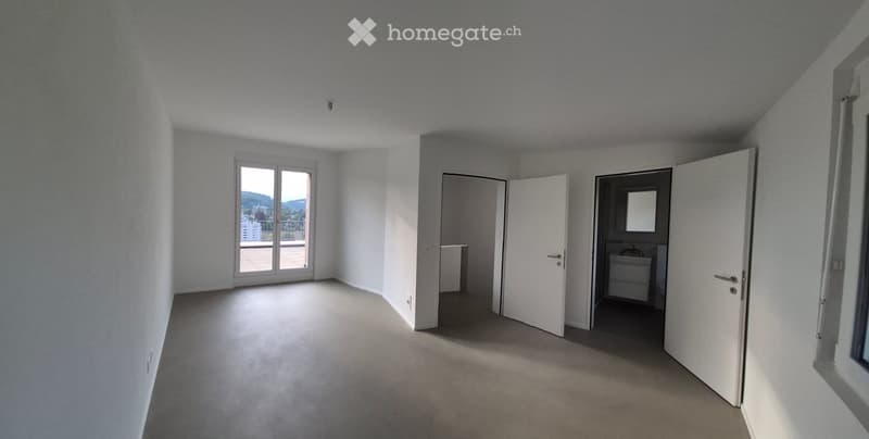 Empty room with white walls, carpeted floor, large window with view, and open doors leading to other rooms.