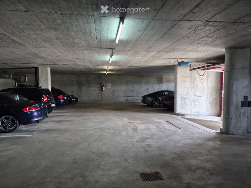 Underground parking area with several parked cars, concrete pillars, and overhead lighting.