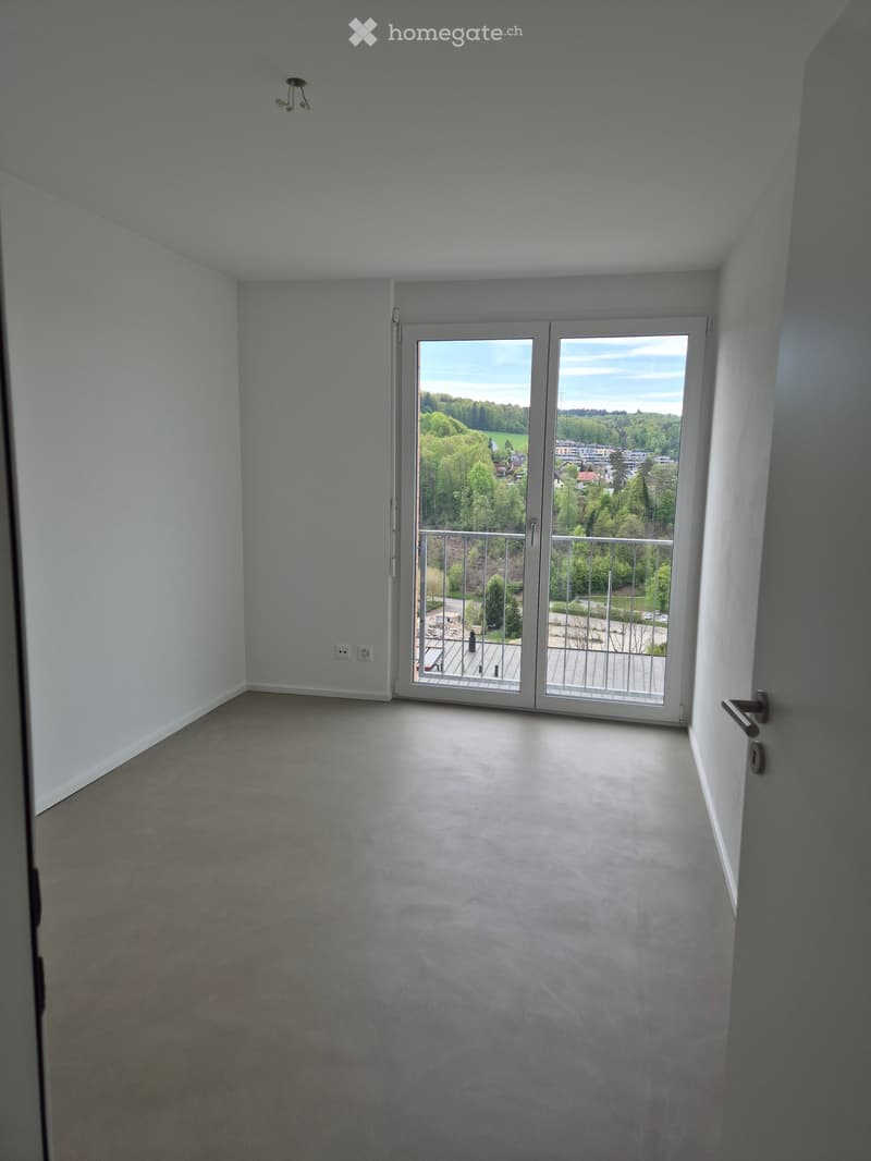 Empty room with light grey walls, carpeted floor, and large sliding glass doors leading to a balcony with a metal railing and outdoor view.