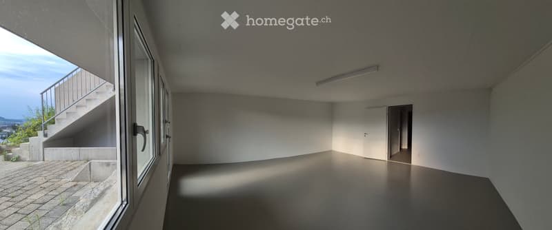 Empty room with bare walls, concrete floor, large window, and a door leading to another space.