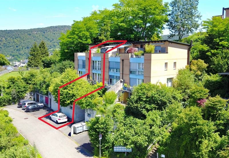 Aerial view of a modern multi-story residential building surrounded by lush greenery, with a garage and parking area visible.