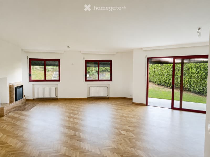 Empty room with wooden herringbone flooring, white walls, large windows, and a sliding glass door leading to a garden.