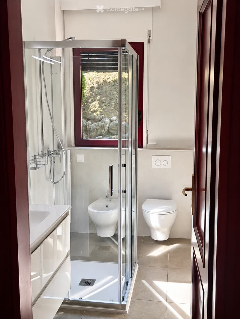 Modern bathroom with a glass-enclosed shower, bathtub, toilet, and bidet. Features a large window with a view of a rocky exterior.