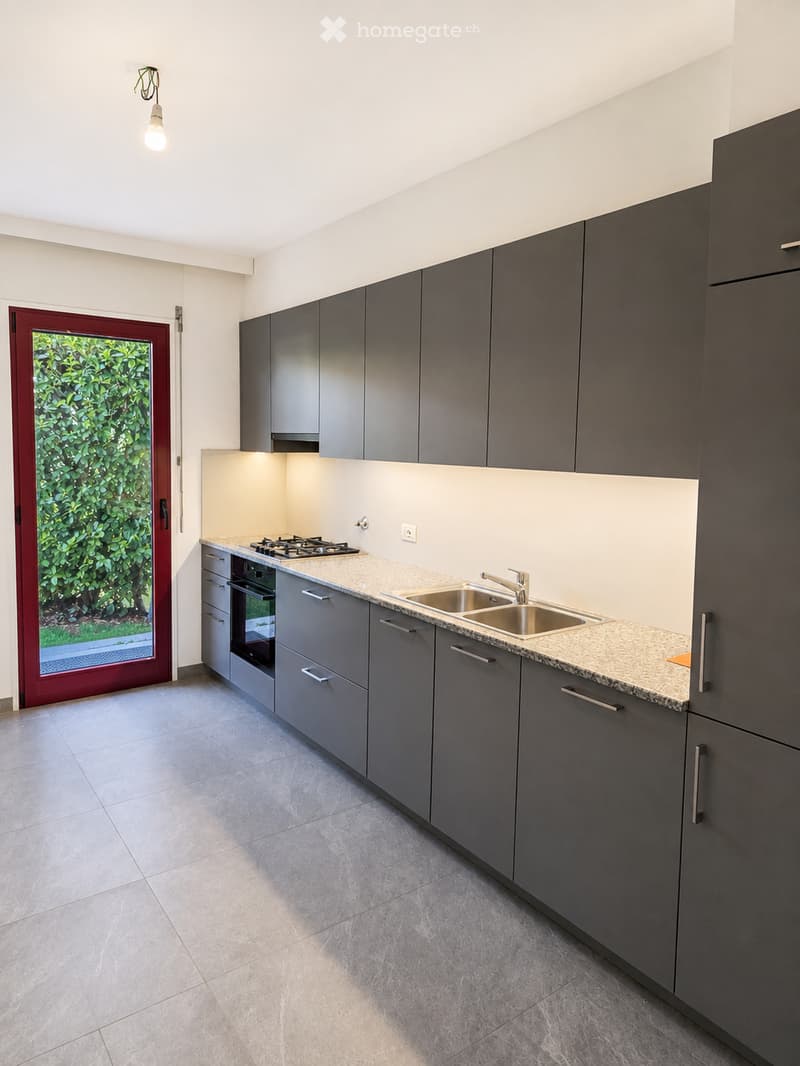 Modern kitchen with grey cabinets, a stainless steel sink, gas stove, and oven. The countertops are light-colored, and the floor is tiled.