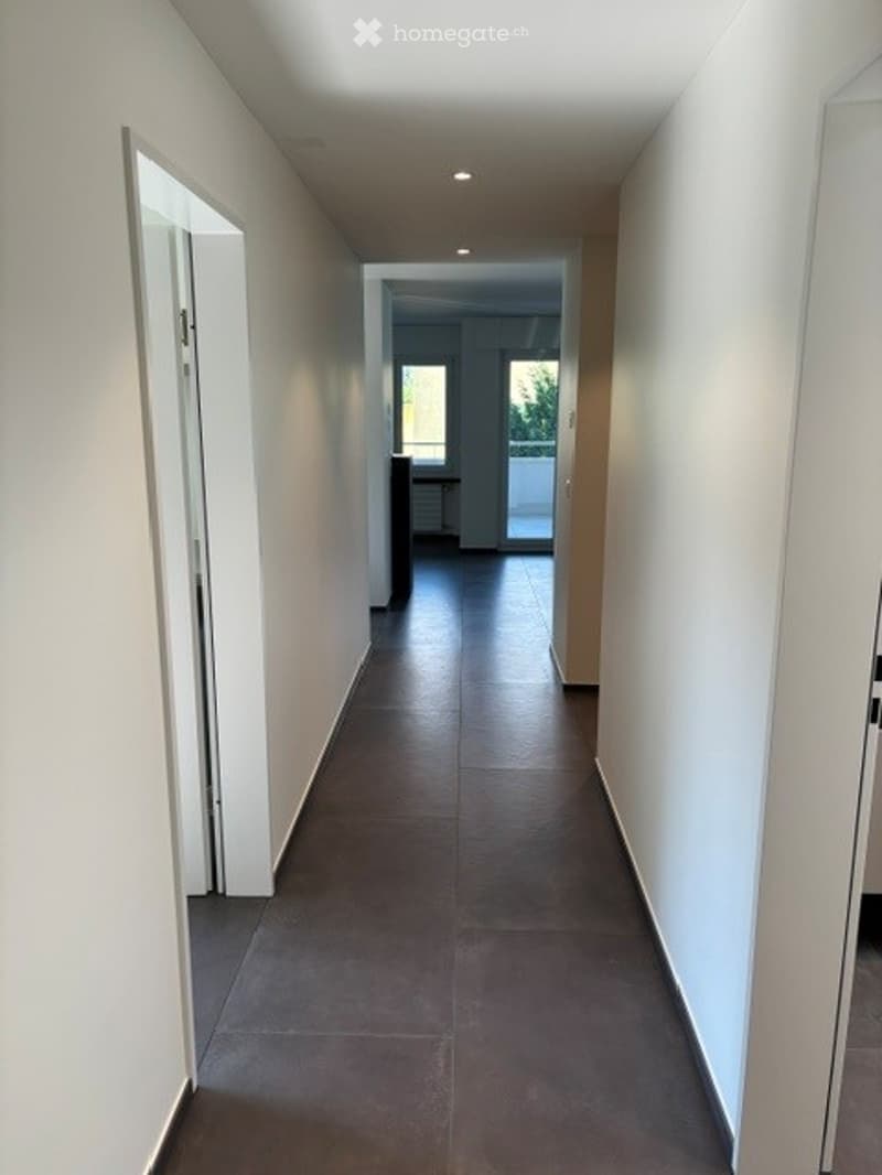 Clean, modern hallway with dark tiled flooring, white walls, and recessed lighting. Doors on both sides lead to other rooms.