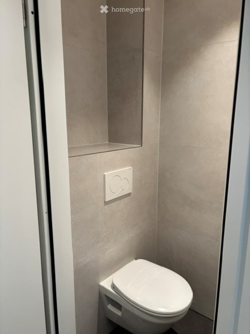 Modern, compact bathroom with beige tiled walls and a white toilet.