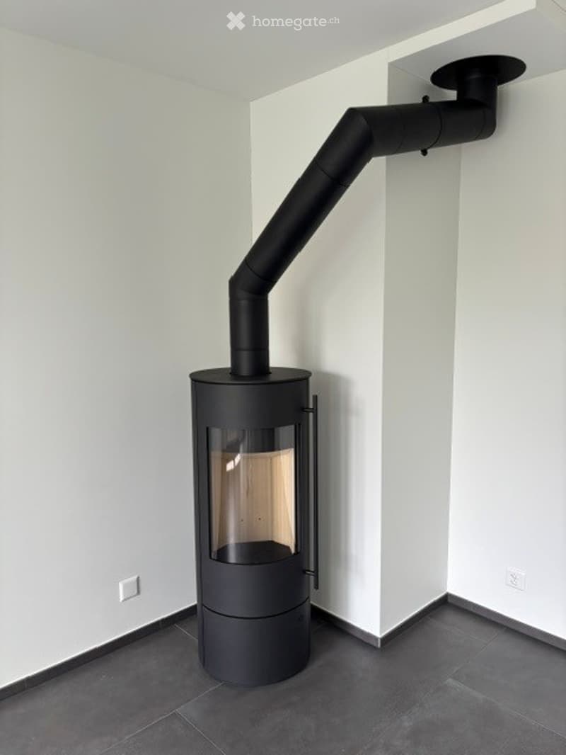 Modern black wood-burning stove with a sleek design, mounted on a dark grey tiled floor against white walls.