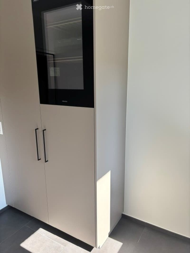 Empty room with white walls, grey tiled floor, and a built-in cabinet with a microwave above it.